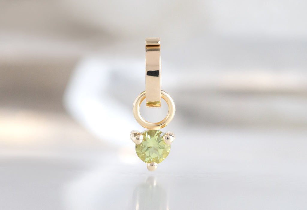 10k Yellow Gold Peridot Birthstone Charm on White Marble Tile