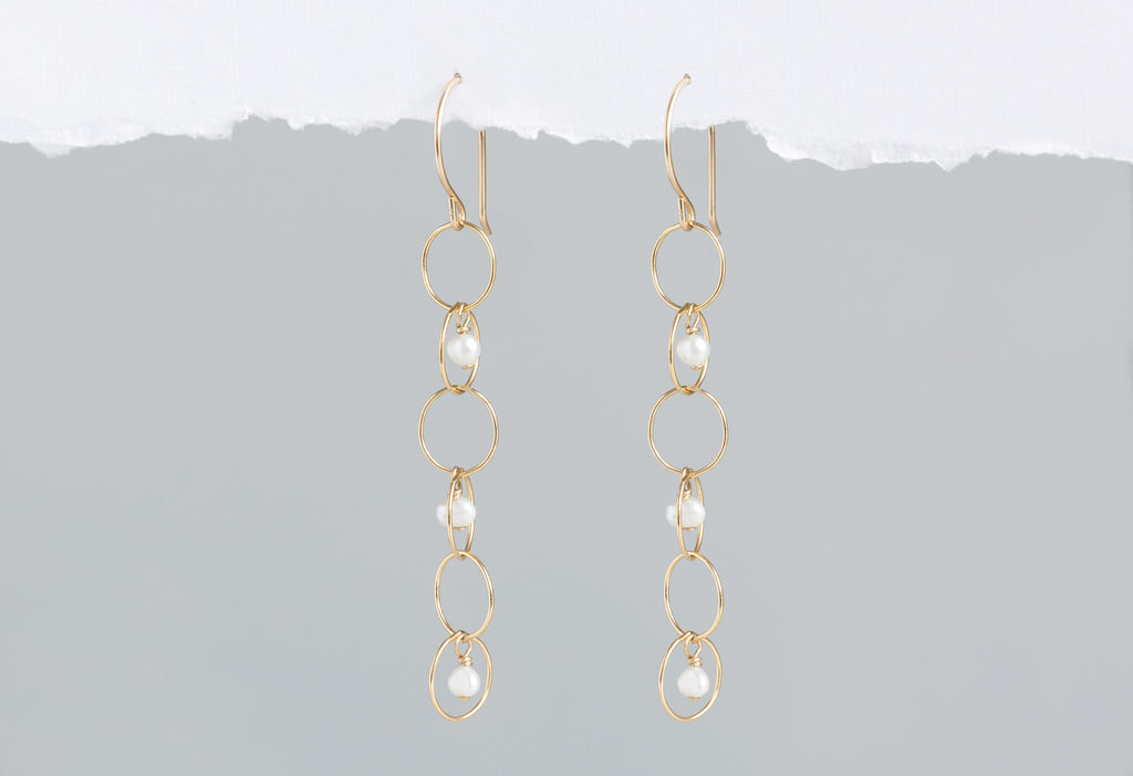 Pearl Party Drop Earrings hanging on white textured paper