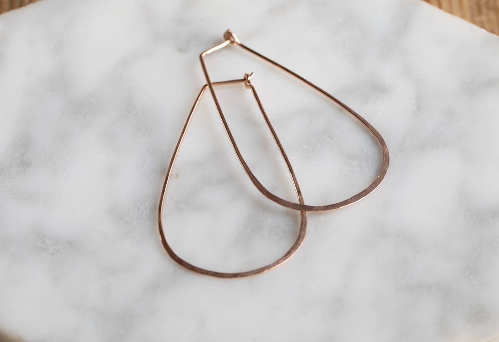 Rose Gold Large Horseshoe Hoop Earrings laying on white marble tile