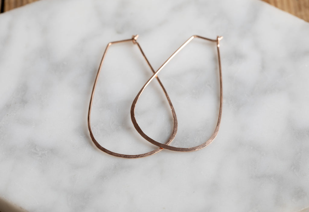 Rose Gold Large Horseshoe Hoop Earrings laying flat on white marble tile