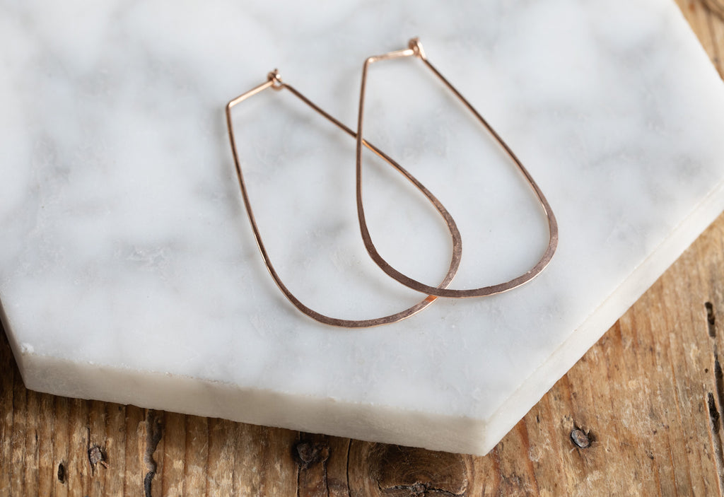 Rose Gold Large Horseshoe Hoop Earrings Laying Flat on White Marble Tile