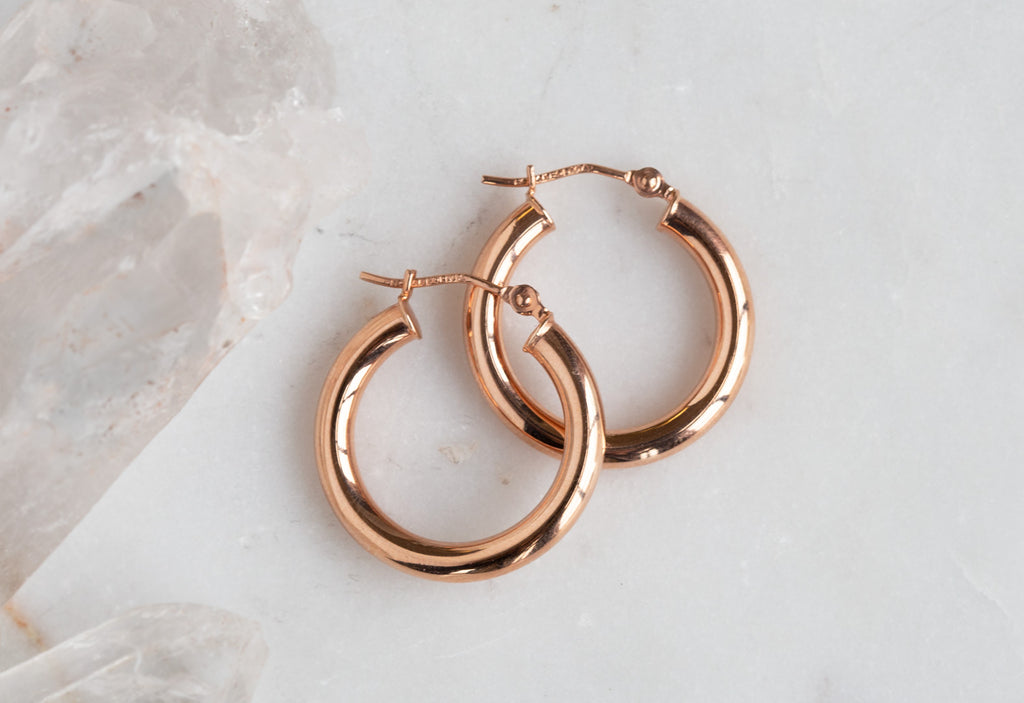 Small Rose Gold Hoop Earrings on white marble tile